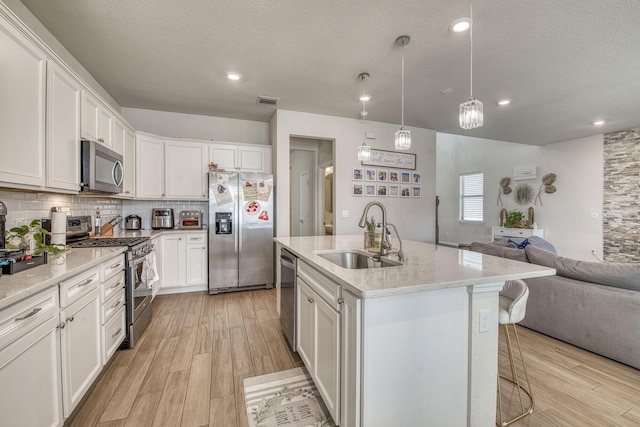 kitchen with tasteful backsplash, appliances with stainless steel finishes, open floor plan, a sink, and light wood-type flooring