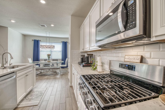 kitchen with light wood finished floors, a sink, stainless steel appliances, white cabinetry, and backsplash