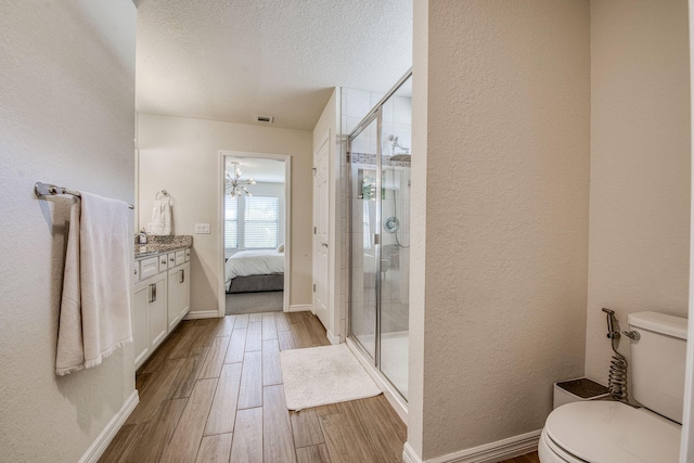 ensuite bathroom with a textured ceiling, a textured wall, toilet, wood finished floors, and a shower stall