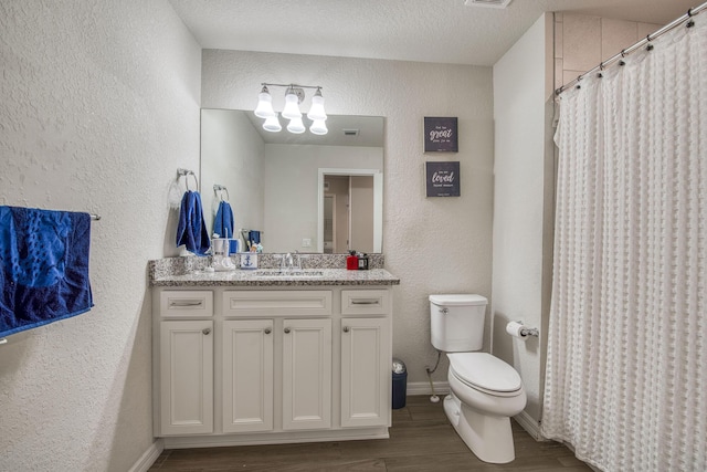 full bathroom featuring a textured wall, toilet, vanity, wood finished floors, and baseboards