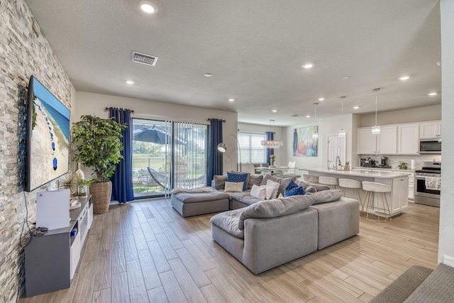 living room featuring a textured ceiling, light wood finished floors, visible vents, and recessed lighting