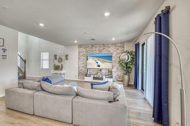 living area featuring a textured ceiling, stairway, light wood-type flooring, and visible vents