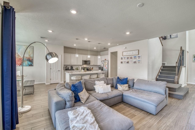 living area featuring light wood-style flooring, stairs, a textured ceiling, and recessed lighting