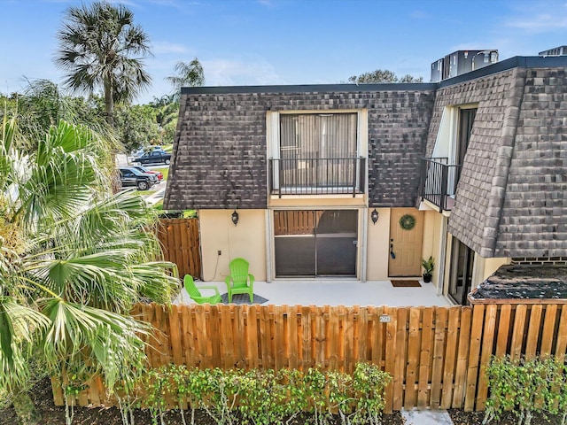 view of front of property featuring a patio, mansard roof, a fenced front yard, a balcony, and stucco siding