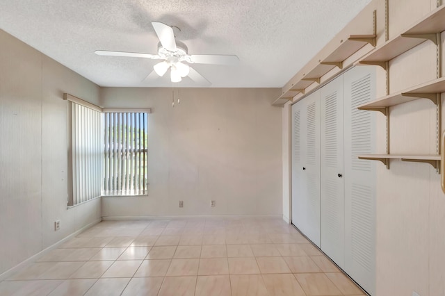 unfurnished bedroom with light tile patterned floors, baseboards, ceiling fan, a textured ceiling, and a closet