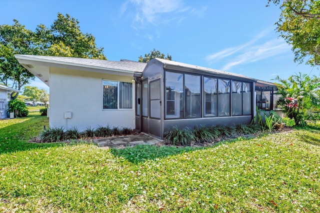 rear view of house featuring a sunroom, a lawn, and stucco siding