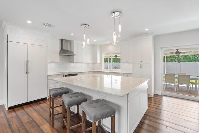 kitchen with wall chimney exhaust hood, dark wood-type flooring, white cabinetry, and a center island