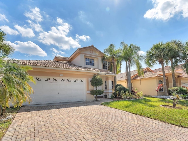 mediterranean / spanish home featuring a tiled roof, an attached garage, decorative driveway, a front lawn, and stucco siding