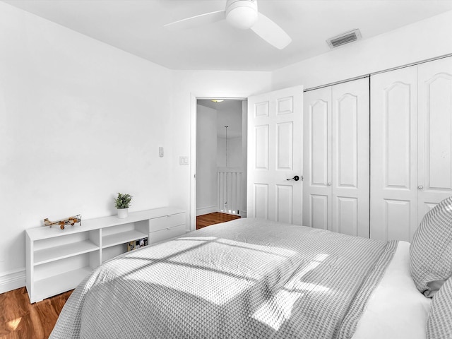 bedroom featuring wood finished floors, visible vents, baseboards, a ceiling fan, and a closet