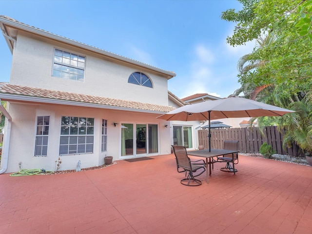 rear view of house featuring a tile roof, fence, a deck, and stucco siding