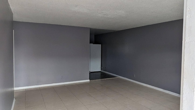 tiled spare room featuring a textured ceiling and baseboards