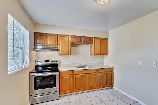 kitchen featuring brown cabinetry, under cabinet range hood, light countertops, stainless steel range with electric stovetop, and a sink