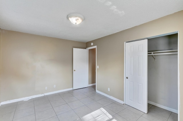 unfurnished bedroom featuring a closet, a textured ceiling, baseboards, and light tile patterned floors