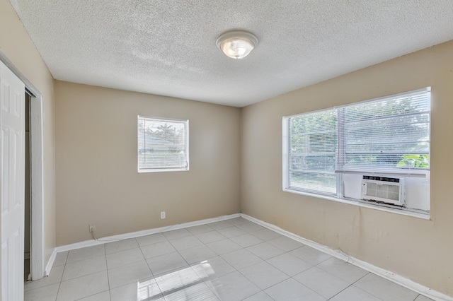 tiled spare room featuring a textured ceiling, cooling unit, a wealth of natural light, and baseboards