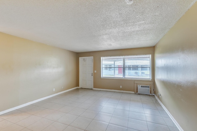 unfurnished room with light tile patterned floors, a textured ceiling, a wall mounted air conditioner, and baseboards