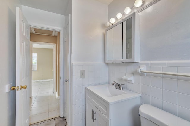 half bathroom with toilet, a wainscoted wall, tile patterned floors, vanity, and tile walls