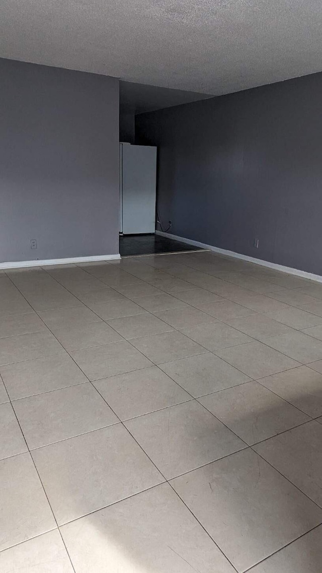 spare room featuring light tile patterned floors, a textured ceiling, and baseboards