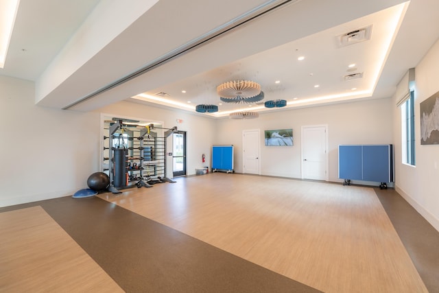 exercise room featuring wood finished floors, a raised ceiling, visible vents, and baseboards