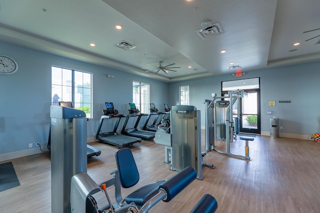 gym with a raised ceiling, visible vents, a ceiling fan, wood finished floors, and baseboards