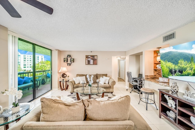 living area with visible vents, a ceiling fan, expansive windows, a textured ceiling, and light tile patterned flooring