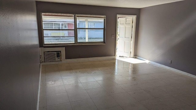 spare room with a wall mounted air conditioner, a textured ceiling, and baseboards