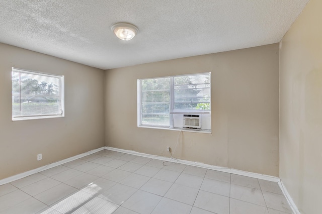 empty room with a textured ceiling, light tile patterned floors, cooling unit, and baseboards