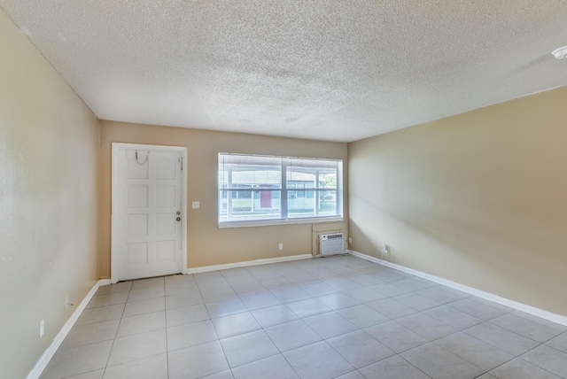 spare room with light tile patterned floors, a textured ceiling, baseboards, and an AC wall unit