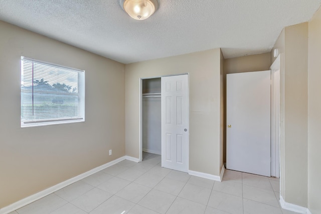 unfurnished bedroom with light tile patterned floors, a textured ceiling, baseboards, and a closet