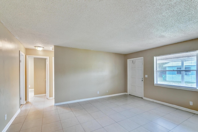 empty room featuring light tile patterned floors, baseboards, and a textured ceiling