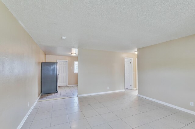 empty room featuring light tile patterned floors, a textured ceiling, and baseboards