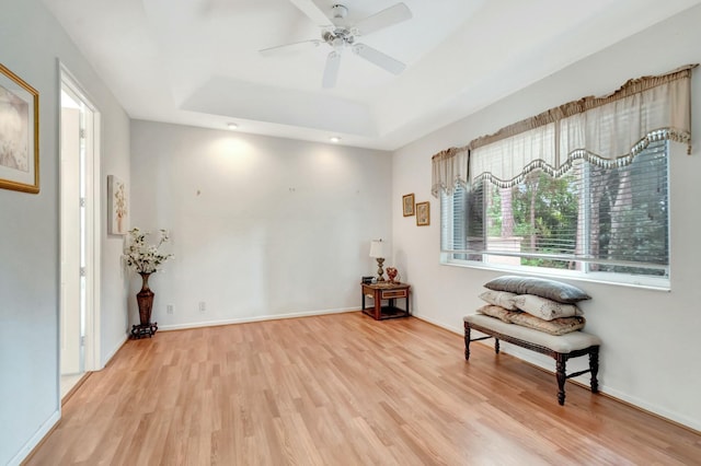 living area featuring a ceiling fan, a raised ceiling, baseboards, and wood finished floors