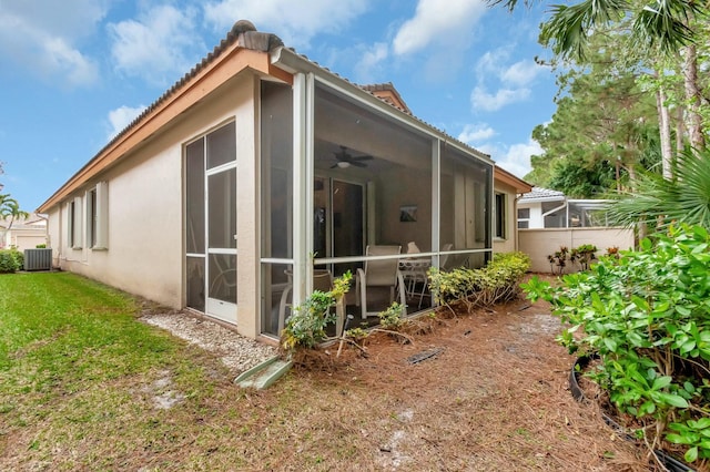 view of home's exterior featuring a sunroom, central AC unit, a lawn, and stucco siding