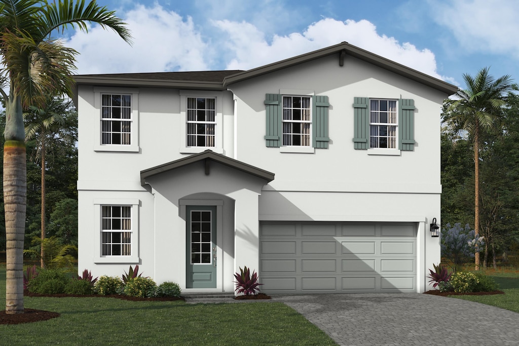 traditional-style home featuring a garage, a front yard, decorative driveway, and stucco siding