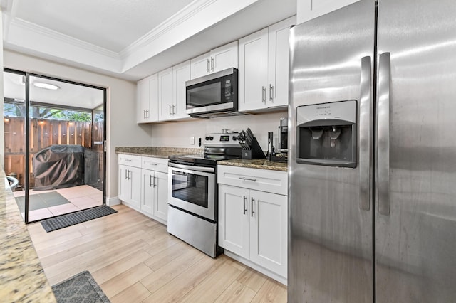 kitchen with dark stone countertops, light wood-style floors, appliances with stainless steel finishes, white cabinetry, and crown molding