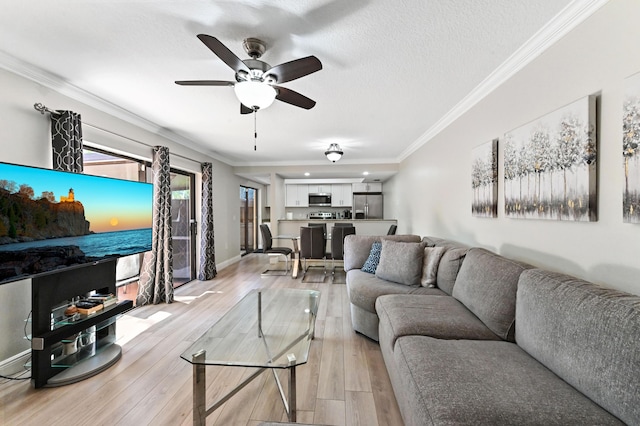 living room with baseboards, ceiling fan, a textured ceiling, crown molding, and light wood-type flooring