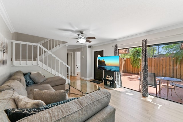 living room with ornamental molding, a ceiling fan, a textured ceiling, wood finished floors, and stairs