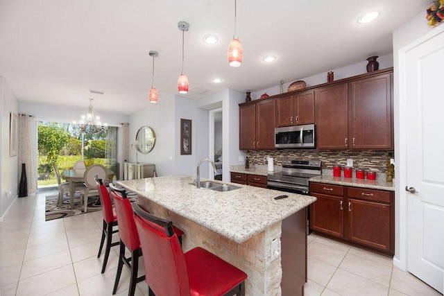 kitchen with light stone counters, light tile patterned flooring, a sink, appliances with stainless steel finishes, and backsplash