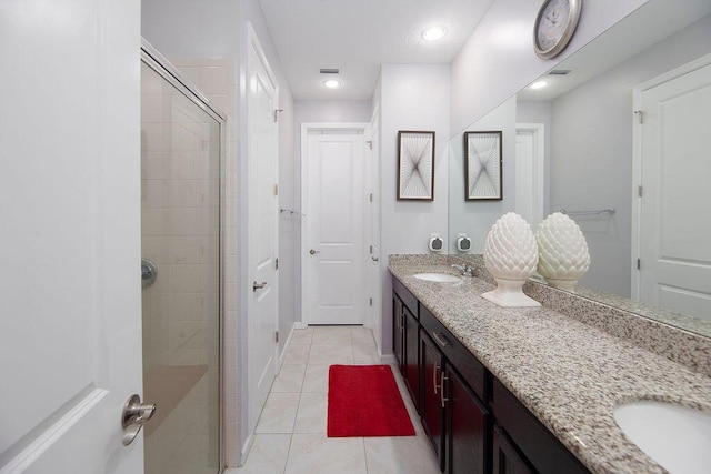 full bath with double vanity, a sink, a shower stall, baseboards, and tile patterned floors