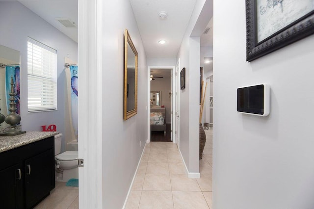 hallway with light tile patterned floors, visible vents, and baseboards