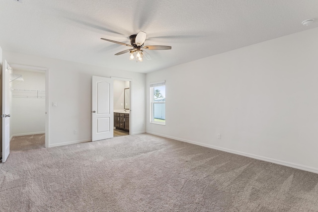 unfurnished bedroom featuring baseboards, a closet, a textured ceiling, a walk in closet, and light carpet