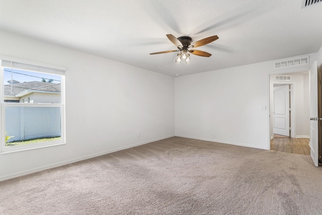 carpeted spare room with visible vents, baseboards, and ceiling fan