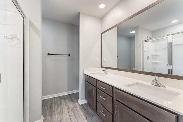 bathroom with double vanity, a shower stall, wood finished floors, and a sink