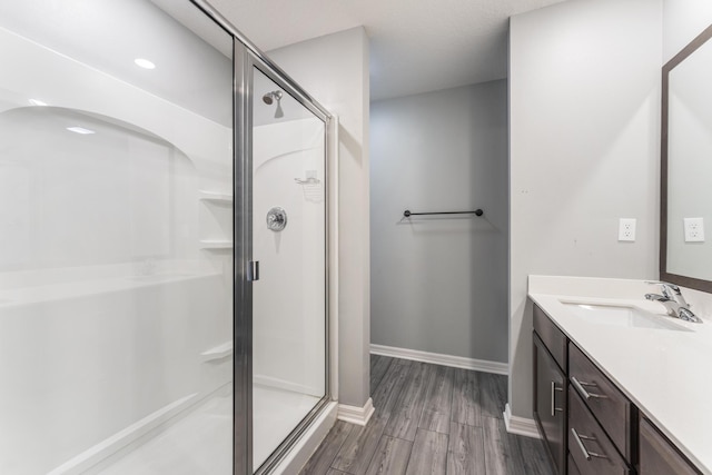 full bath featuring a stall shower, vanity, baseboards, and wood finished floors