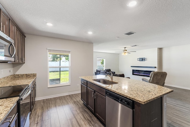 kitchen with dark wood-style floors, stainless steel appliances, a sink, open floor plan, and a large fireplace