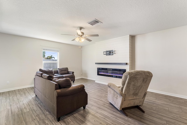 living area with visible vents, a textured ceiling, a glass covered fireplace, wood finished floors, and baseboards