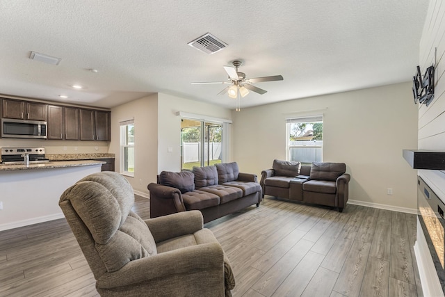 living area featuring visible vents, baseboards, a textured ceiling, and wood finished floors