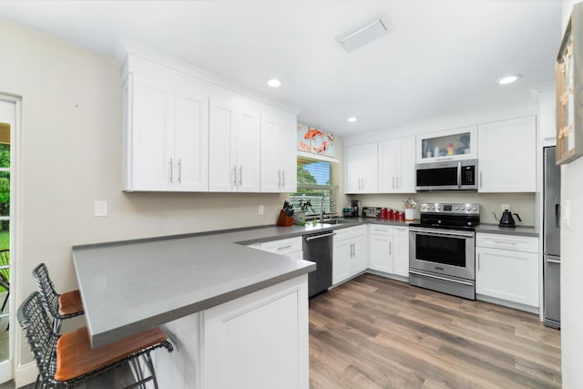 kitchen with stainless steel appliances, a peninsula, a sink, visible vents, and white cabinets