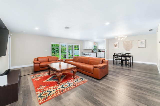 living room featuring an inviting chandelier, visible vents, baseboards, and wood finished floors