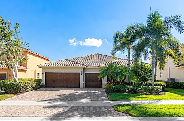 mediterranean / spanish house featuring a tiled roof, decorative driveway, an attached garage, and stucco siding