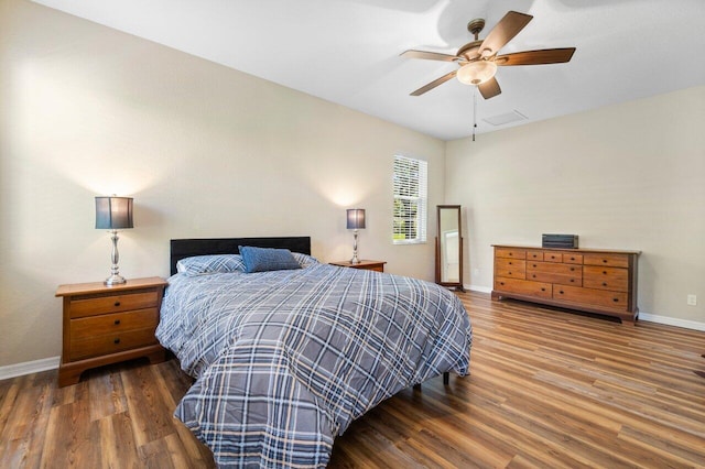 bedroom with a ceiling fan, visible vents, baseboards, and wood finished floors